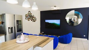 A modern kitchen with a Samsung refrigerator, a wooden dining table with a pink coffee maker, and a blue sofa.