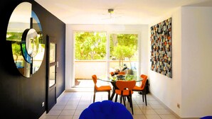 A modern dining area with a glass table, orange chairs, and a view of greenery outside.