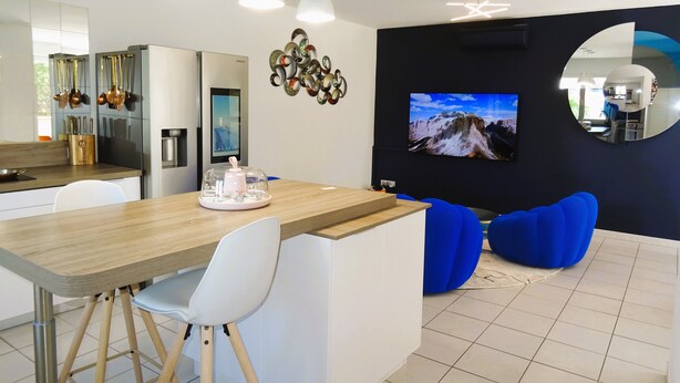 A modern kitchen with a wooden island, white chairs, and a dining area with blue bean bag chairs.