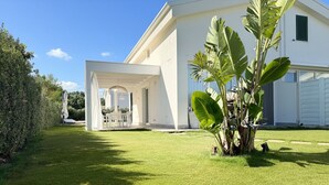 Una casa moderna con patio coperto, prato curato e un'ampia pianta in primo piano.