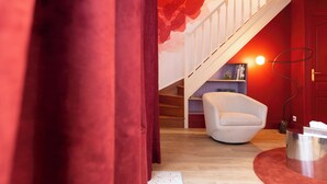 Ein Zimmer mit roter Wand, weißem Stuhl, einer Holztreppe und einem Bücherregal.