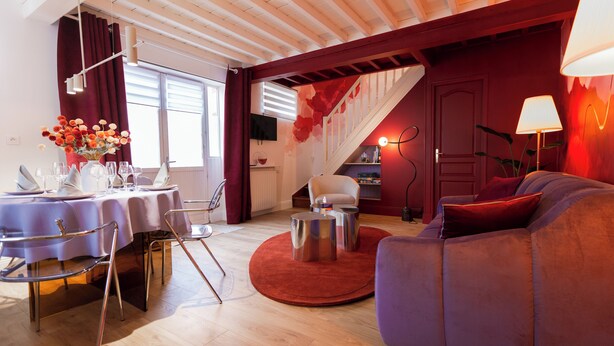 Ein modernes Wohnzimmer mit Essbereich, ausgestattet mit einer Couch, Sesseln, einem runden Esstisch und einer Treppe, die in eine obere Ebene führt.