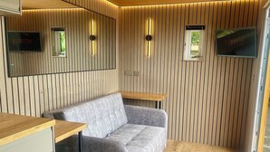 A modern room with a grey sofa, wooden panel walls, and two wall-mounted TVs. - Beautiful beachside cabin perfect for a relaxing getaway (Skegness)