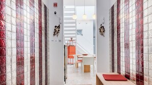 Ein Korridor mit Fischgrätparkett, rot-weißen Fliesenwänden und einer Holzbank mit roten Kissen.