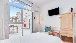 Ein modernes Hotelzimmer mit einem großen Bett, einem an der Wand befestigten Fernseher, einem Holzschrank und einem Balkon mit Tisch und Stühlen.