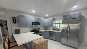 Una cocina moderna con armarios grises, electrodomésticos de acero inoxidable, encimera blanca e isla de madera con asientos.