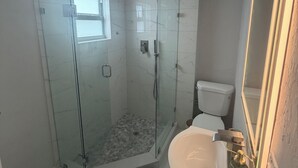 Un baño con ducha vidriada, inodoro, lavamanos y espejo.