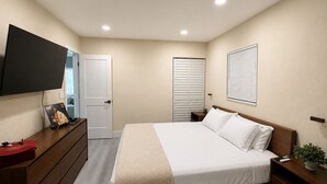 Un dormitorio con cama, cómoda, mesita de noche, televisor, armario y persianas.