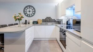 Eine moderne Küche mit weißen Schränken, einer großen Uhr und einer Vase mit Blumen.