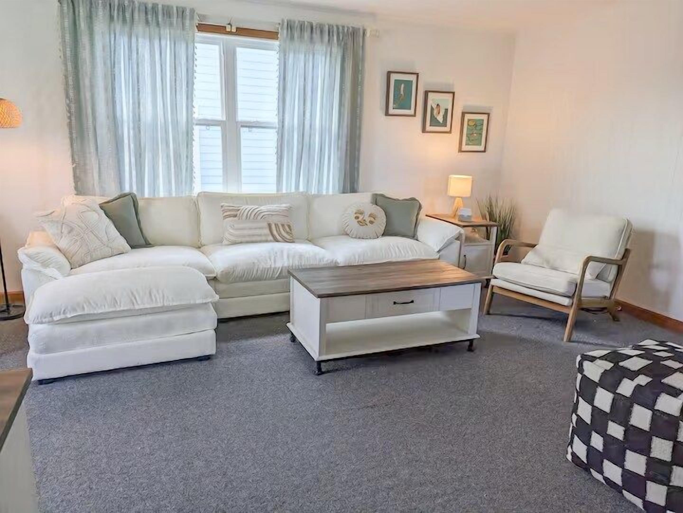 Una sala de estar con un sofá, una mesa de centro, una silla y un pequeño reposapiés.