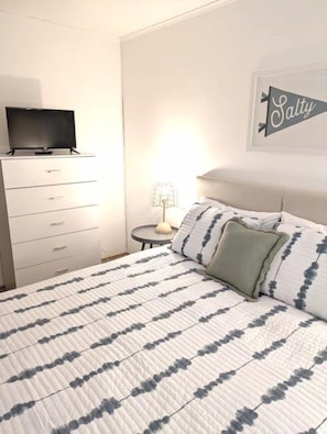 A bedroom with a bed, a dresser, a television on top, a lamp, and a wall sign.