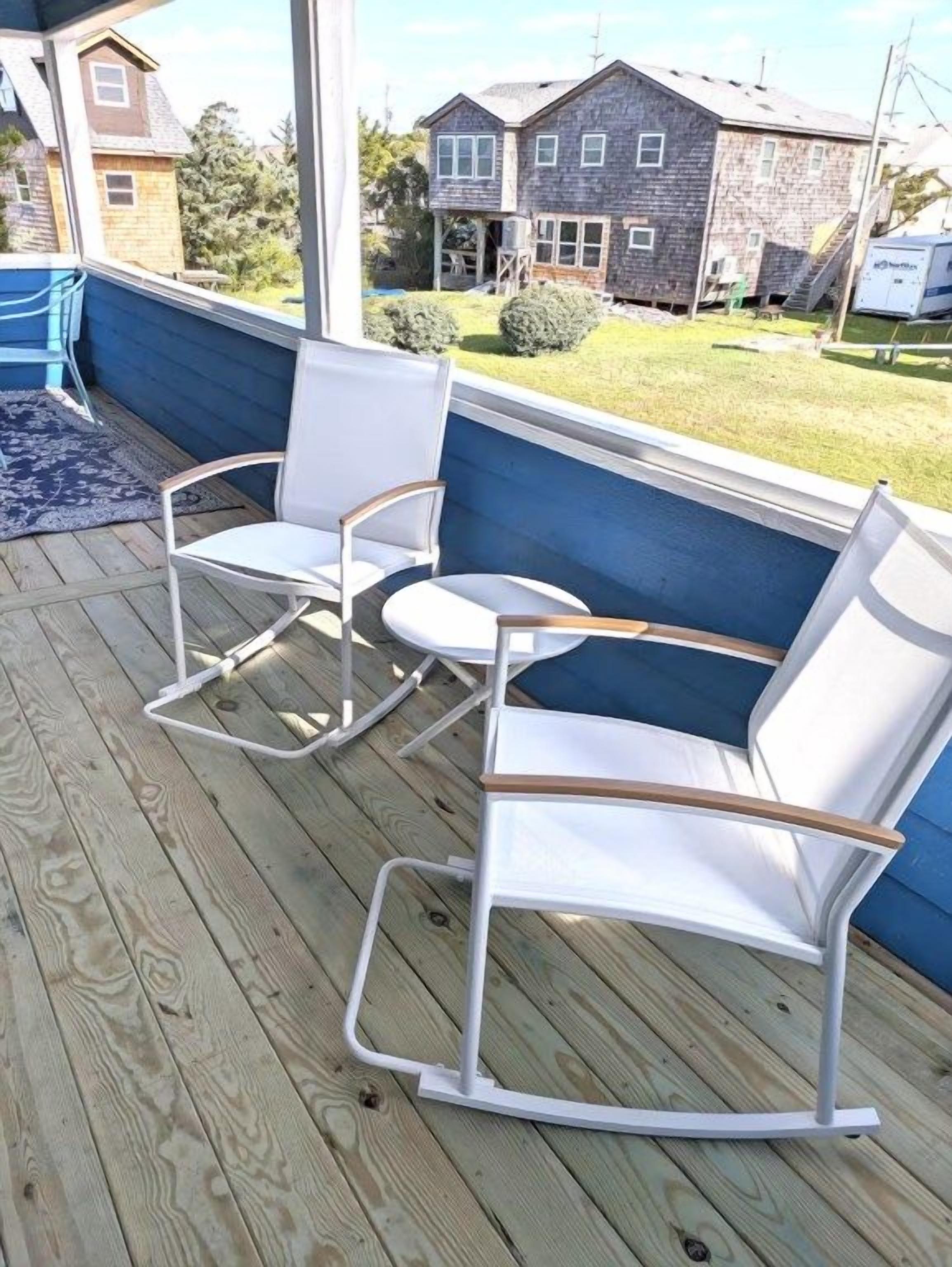 Une terrasse en bois avec un mur bleu et une chaise berçante blanche.