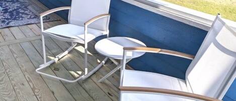 A wooden deck with a blue wall and a white rocking chair.