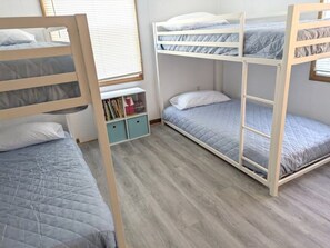 A room with bunk beds, a small storage unit, and a window with blinds.