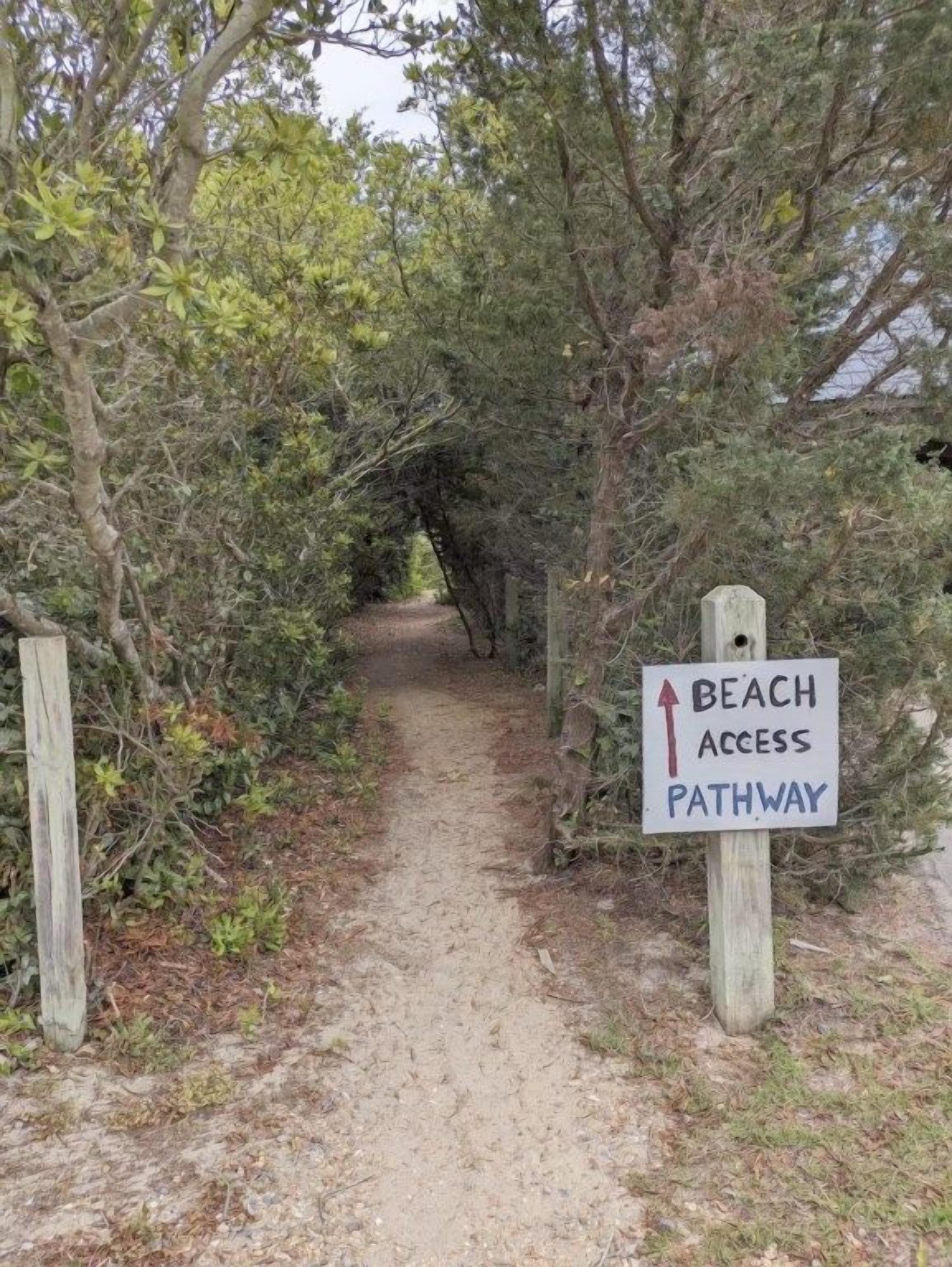 Ein unbefestigter Pfad mit einem Schild, das den Zugang zum Strand anzeigt.