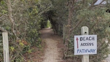 Un sentier de terre avec un panneau indiquant l’accès à la plage.