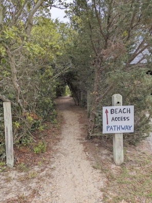 Un sendero de tierra con un letrero que indica acceso a la playa.