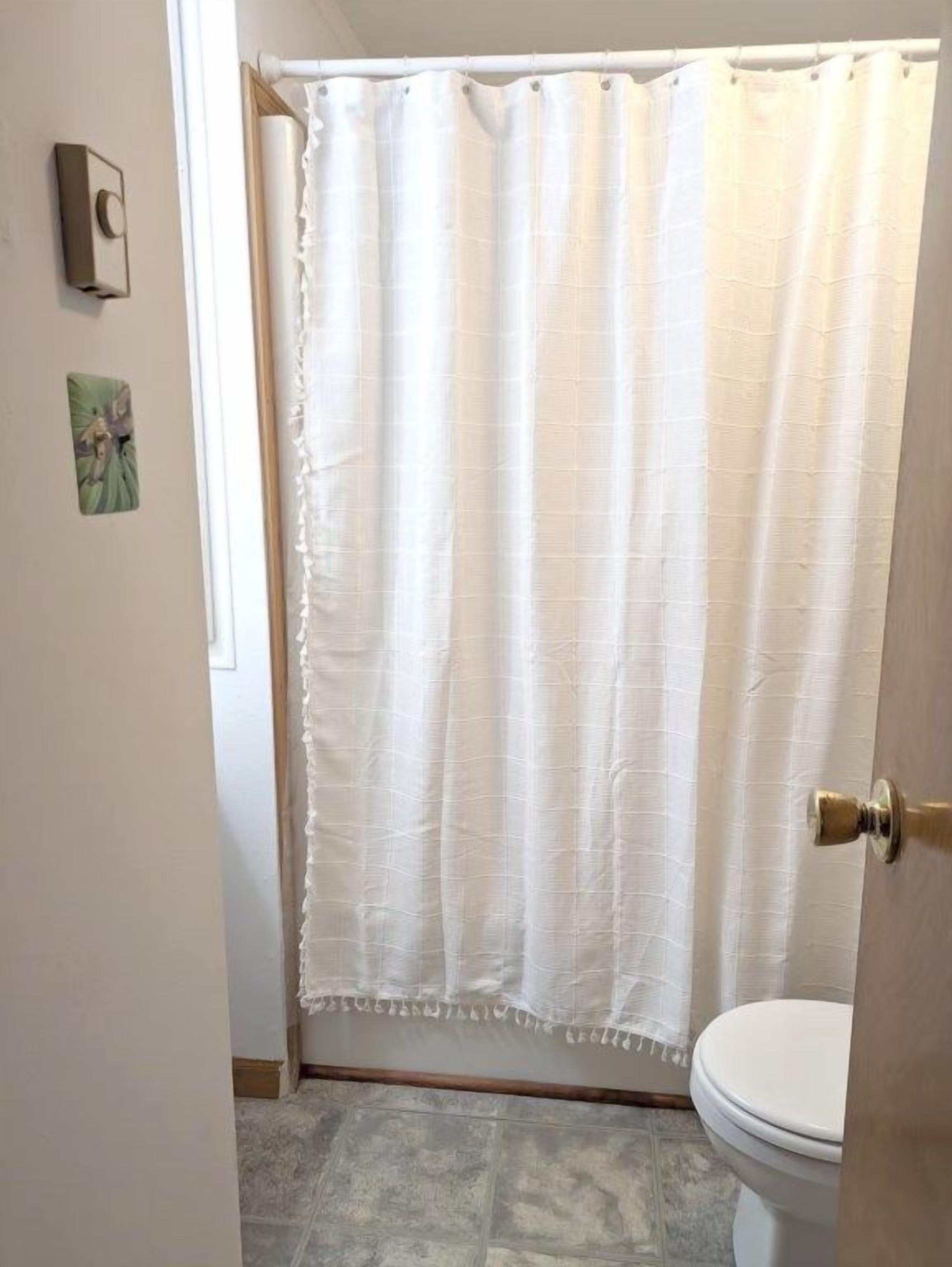 Un baño con cortina blanca de ducha, un inodoro y una puerta con pomo de latón.