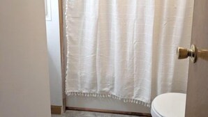 Une salle de bain avec un rideau de douche blanc, des toilettes et une porte dotée d’une poignée en laiton.