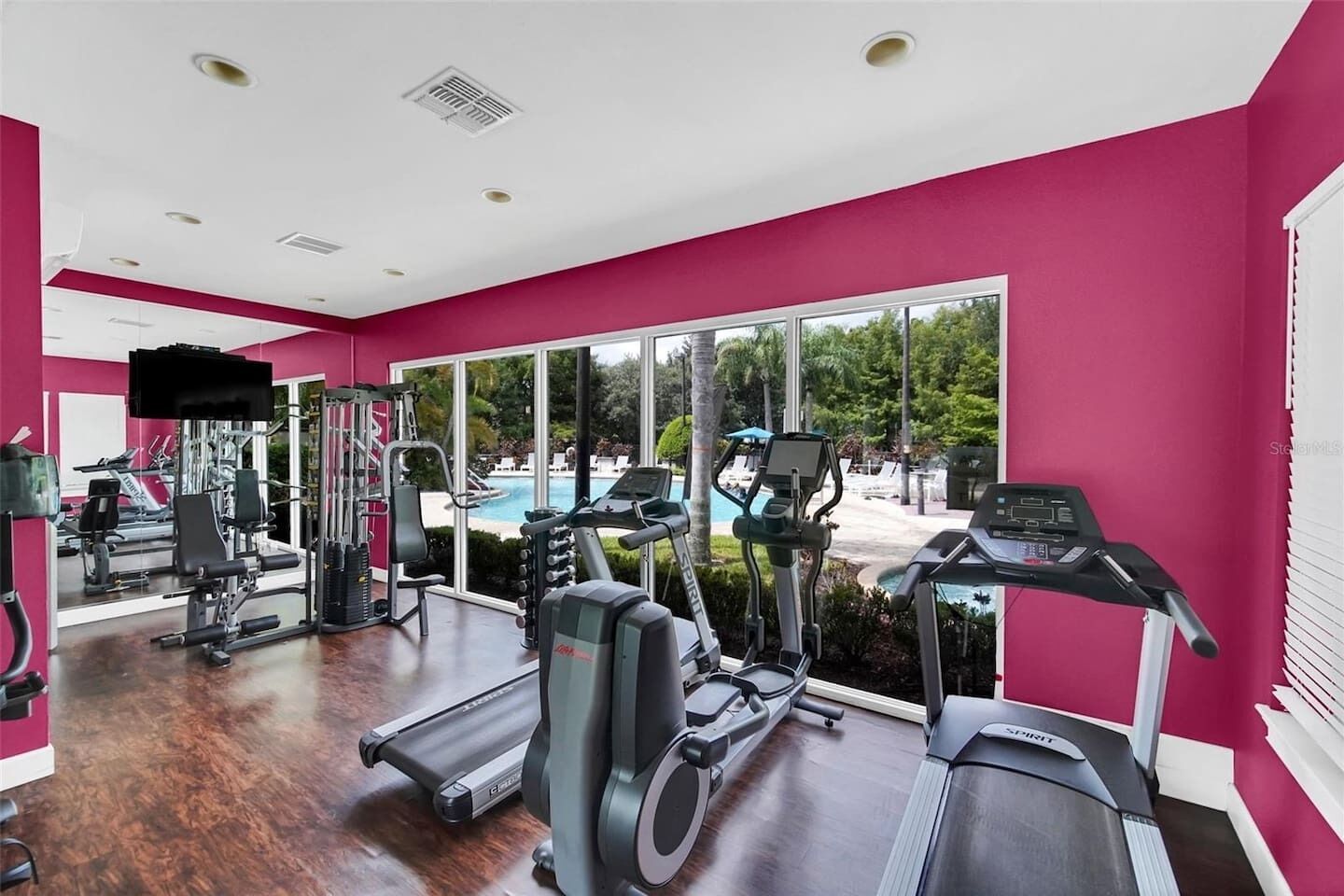 A gym with cardio machines, weight training equipment, and a large window overlooking a pool.