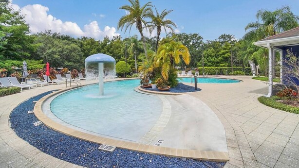 A swimming pool with a water fountain, surrounded by lounge chairs and palm trees. - Resort Townhome Minutes to Disney (Kissimmee)