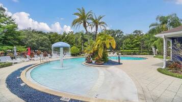 A swimming pool with a water fountain, surrounded by lounge chairs and palm trees.