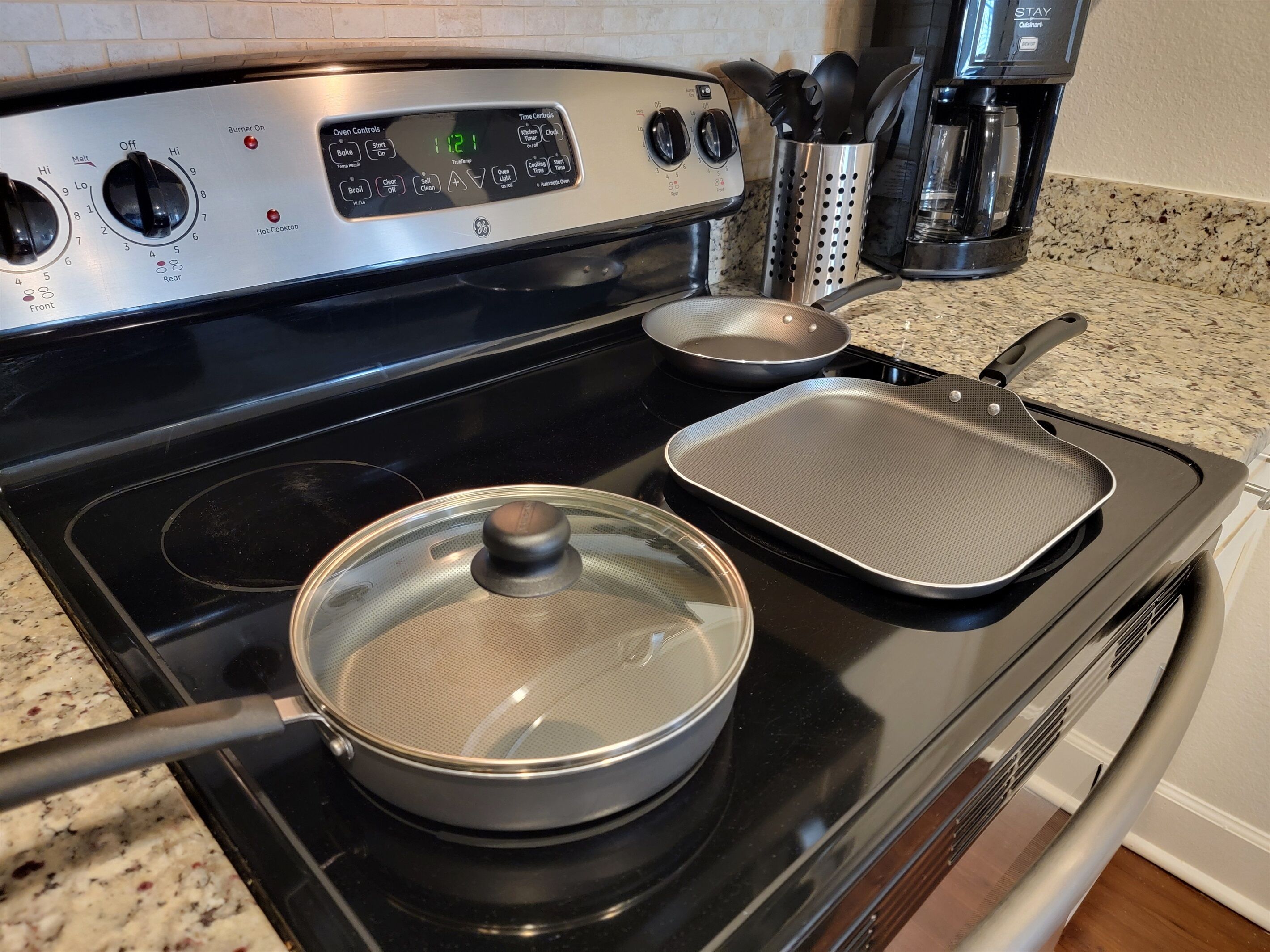 Una cocina con estufa, una olla con tapa, una sartén y una cafetera.