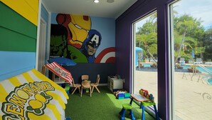 A children's playroom with a mural, green artificial turf, and a view of a swimming pool. - Resort Townhome Minutes to Disney (Kissimmee)