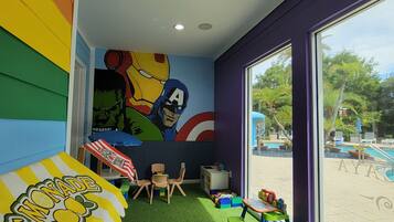 Ein Spielzimmer für Kinder mit Wandgemälde, grünem Kunstrasen und Blick auf einen Swimmingpool.