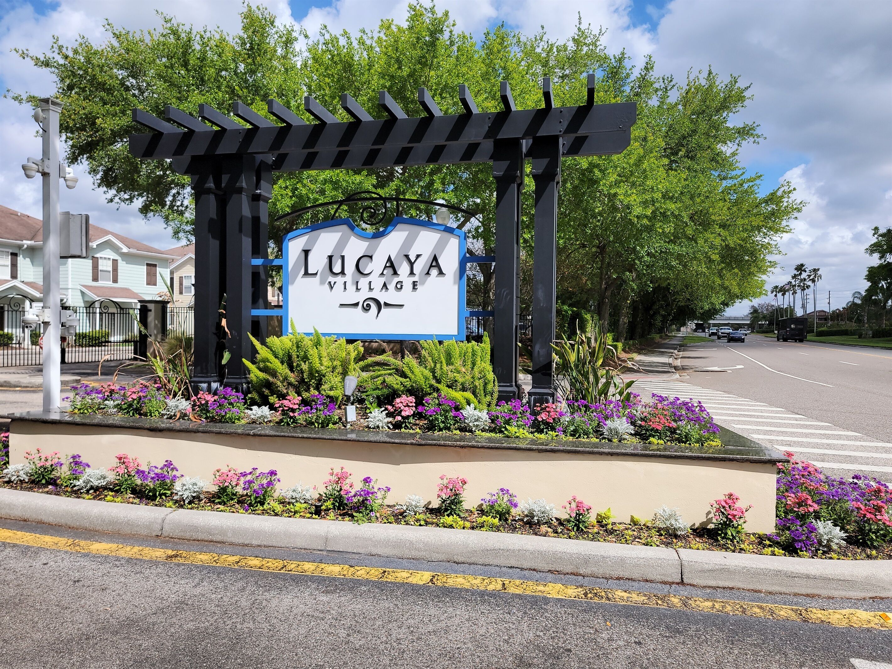 A sign for Lucaya Village with a pergola and flower beds.