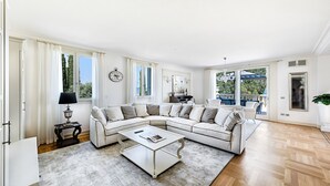 A spacious living room with a large L-shaped sectional sofa, a coffee table, and a view of the outdoors through large windows. - Luxury Lake-Front Catullo A2 (Sirmione)