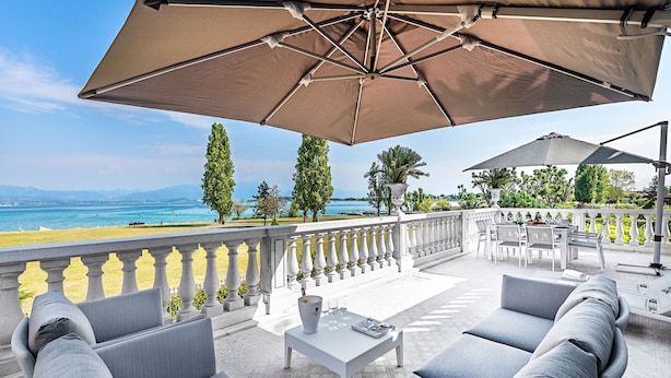 A terrace with outdoor seating, a view of the sea, and a white balustrade. - Luxury Lake-Front Catullo A2 (Sirmione)