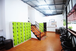A hotel lobby with a staircase, green lockers, a trash bin, and a seating area with chairs. - Slinky Hostel (Ko Phi Phi)