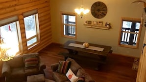 Interior acogedor de una cabaña con techo de madera, dos sofás, una mesa de comedor y un reloj en la pared.