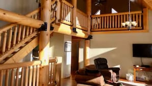 Amplia sala de estar con escalera de madera, zona de estar confortable y televisor.