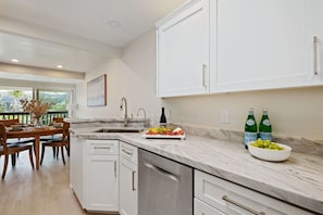A modern kitchen with white cabinets, a marble countertop, and a dining area with a wooden table and chairs. - Montecito Penthouse, 2 + 2, walk to Butterfly Beach & Coast Village Road (Montecito)