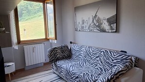 A living room with a zebra-patterned sofa, a radiator, a window with a view of greenery, and a cityscape painting on the wall. - House of the stars (Lombardia)