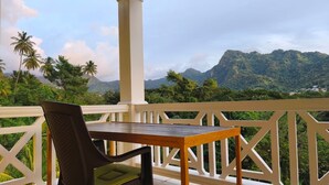 Un balcon avec une table et une chaise, donnant sur un paysage montagneux parsemé de palmiers.