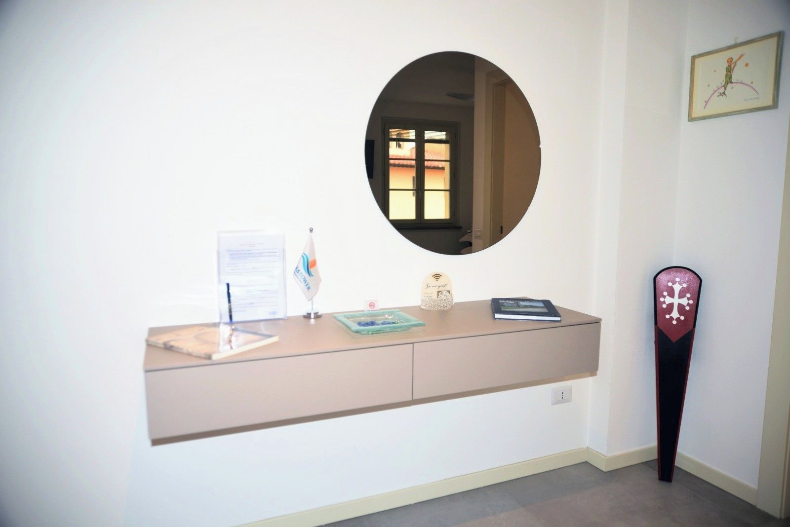 A reception desk with a mirror, a framed picture, and a decorative object on the wall.