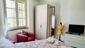 A hotel room with a bed, a red chair, a wardrobe, a mirror, a mannequin, and a television.