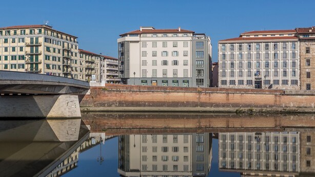A canal with buildings reflecting on the water, a bridge, and a clear sky.