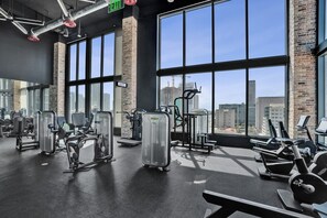 Ein Fitnessstudio mit verschiedenen Trainingsgeräten, großen Fenstern und Blick auf die Stadtlandschaft.