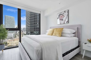 Ein modernes Schlafzimmer mit einem großen Bett, Blick auf die Stadt und einem gerahmten Kunstwerk an der Wand.