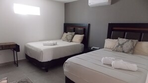 Hotellihuone, jossa on kaksi sänkyä, yöpöytä, matto ja ilmastointilaite.