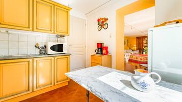 Een keuken met gele kastjes, een witte magnetron, een koffiezetapparaat en een marmeren aanrecht.