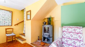 Une pièce comprenant une chaise en bois, un canapé, une petite table avec un pot, un poêle et un miroir fixé au mur.