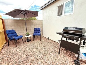An outdoor patio with a barbecue grill, two blue chairs, a small table with a plant, and an umbrella. - Central, close to trails, shopping, downtown (Tucson)