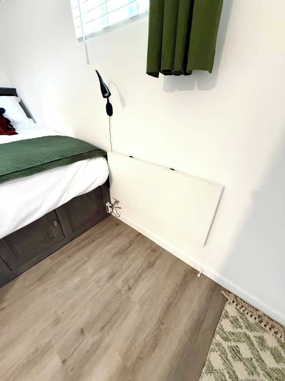 Ein Schlafzimmer mit Bett, Nachttisch, Lampe, Fenster mit Vorhängen und Holzboden.