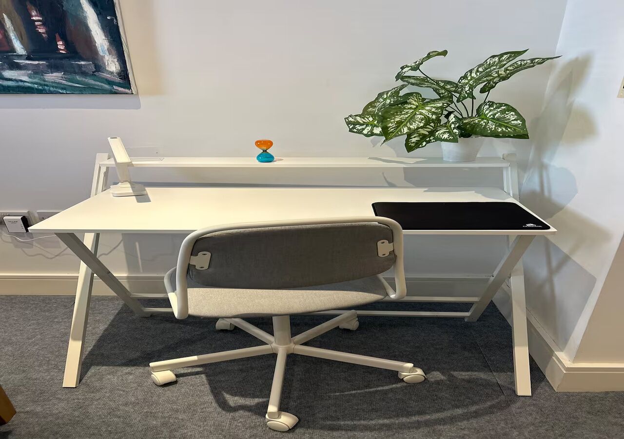 A white desk with a grey office chair, a potted plant, and a small orange and blue object on the shelf.