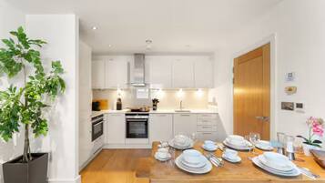 A modern kitchen with white cabinets, a wooden dining table set for four, and a potted plant.